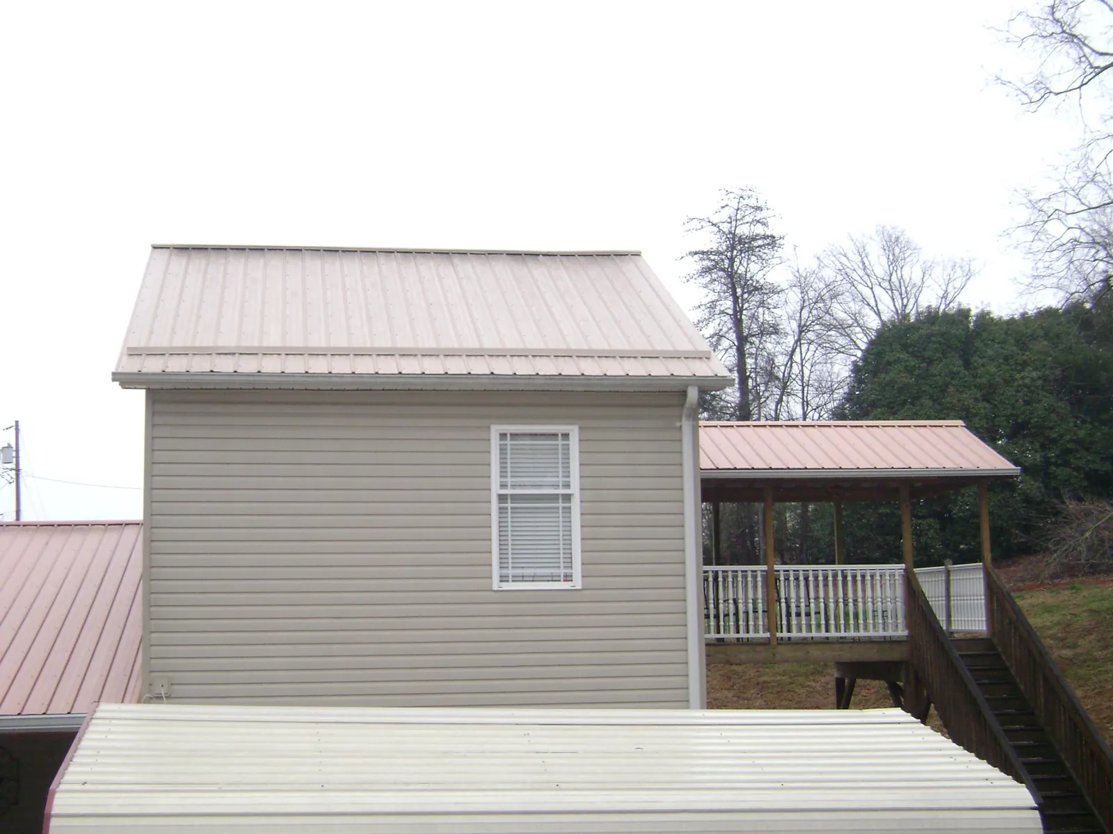 Tan metal roofs on a two story addition and attached porch, from a Roof Replacement job in Carthage